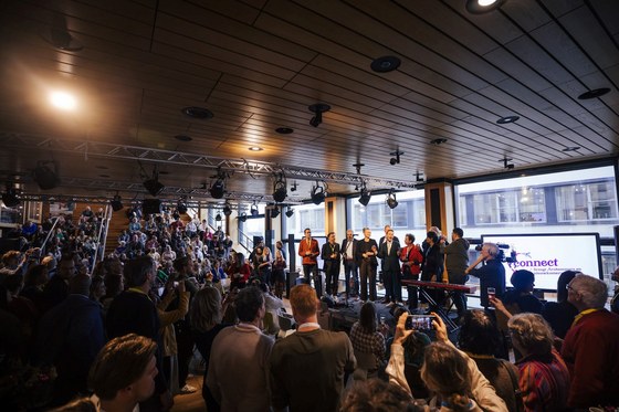 Openingsbijeenkomst van Connect met wethouders Paul Smeulders, Cathelijne Bouwkamp en Bob Roelofs op het podium