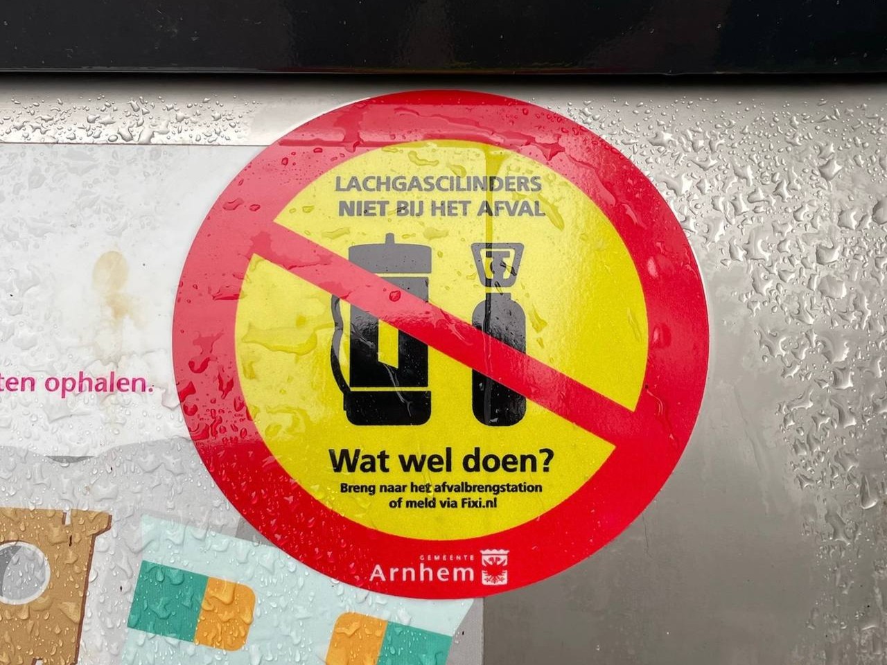 Sticker met de tekst 'Lachgascilinders niet bij het afval. Wat wel doen? Breng naar het afvalbrengstation of meld via Fixi.nl' op container