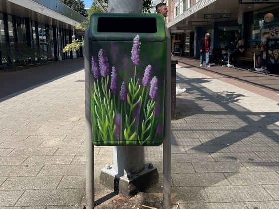 Met bloemen beschilderde prullenbak bij winkelcentrum Drieslag