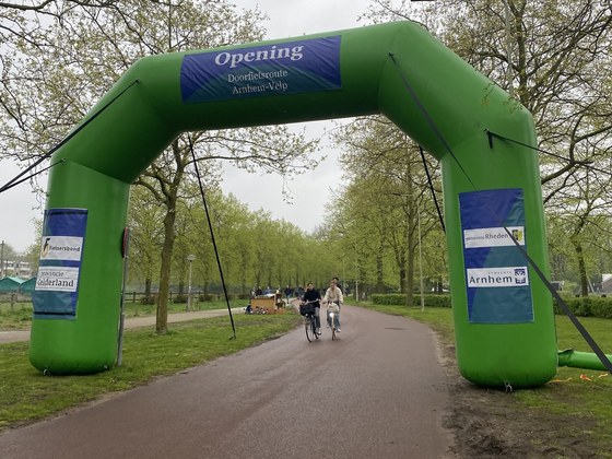 Twee fietsers fietsen onder de groene opblaas startboog door op de nieuwe doorfietsroute