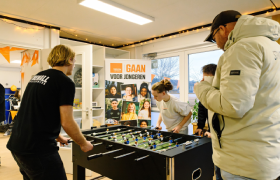 Drie jongeren zijn onder toeziend oog van een begeleider aan het tafelvoetballen.