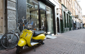 Een gele Vespa scooter staat geparkeerd voor een winkel