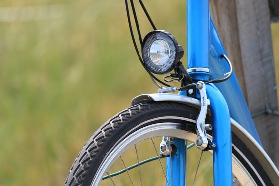 Een close-up van een fiets, de voorlamp en een deel van het voorwiel zijn zichtbaar.