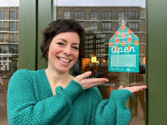 Ondernemer Esther Poelen staat naast het bordje met daarop de tekst 'wees welkom' dat op de ruit van haar winkel hangt.