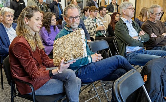 Mensen zitten in een zaal, een vrouw houdt herbruikbaar materiaal vast