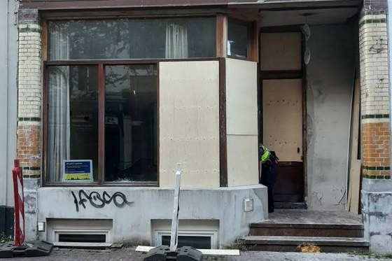 De voorgevel van de woning. Bij een deel van het raam zijn houten panelen bevestigd. Een politiemedewerker doet onderzoek.