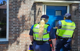 2 handhavers staan voor de deur van een pand