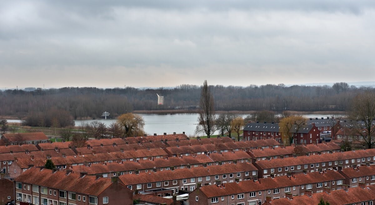 Een luchtfoto met daarop rode daken van een woonwijk in Arnhem, liggend aan het water.