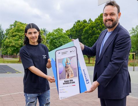 Wethouder Mark Lauriks overhandigt een groot eerste exemplaar van de verjaardagskaart aan Arnhemse Mert (17).