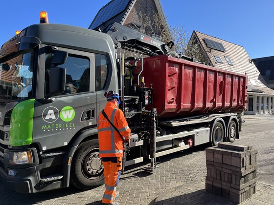Een vrachtwagen met een kraan staat naast een stapel stenen.
